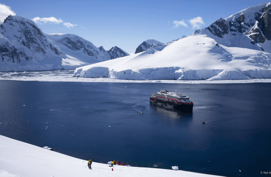 A big ship on the water surrounded by snowy mountains.