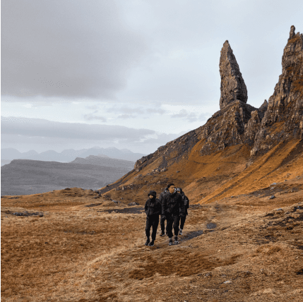 People walking on a path in a park with a rock formation in the background.