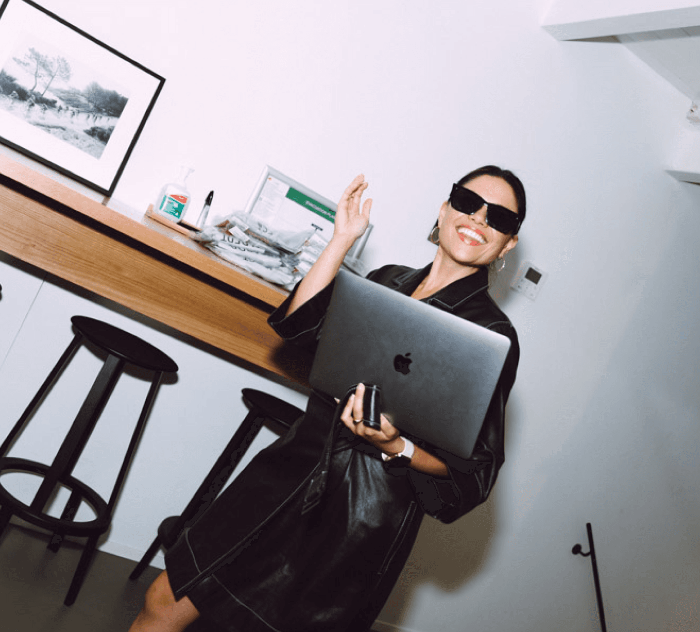 Person smiling with sunglasses on carrying a laptop.